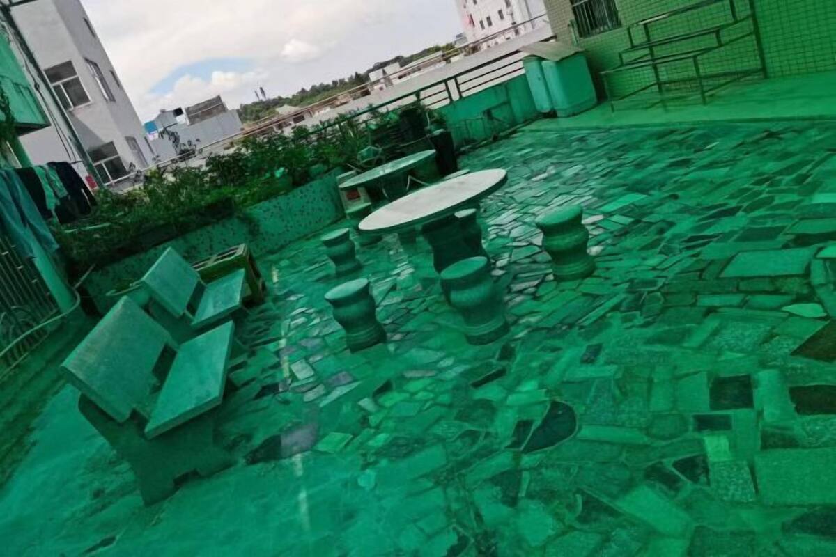 A rooftop terrace with stone flooring, green outdoor furniture, and a view of surrounding buildings.
