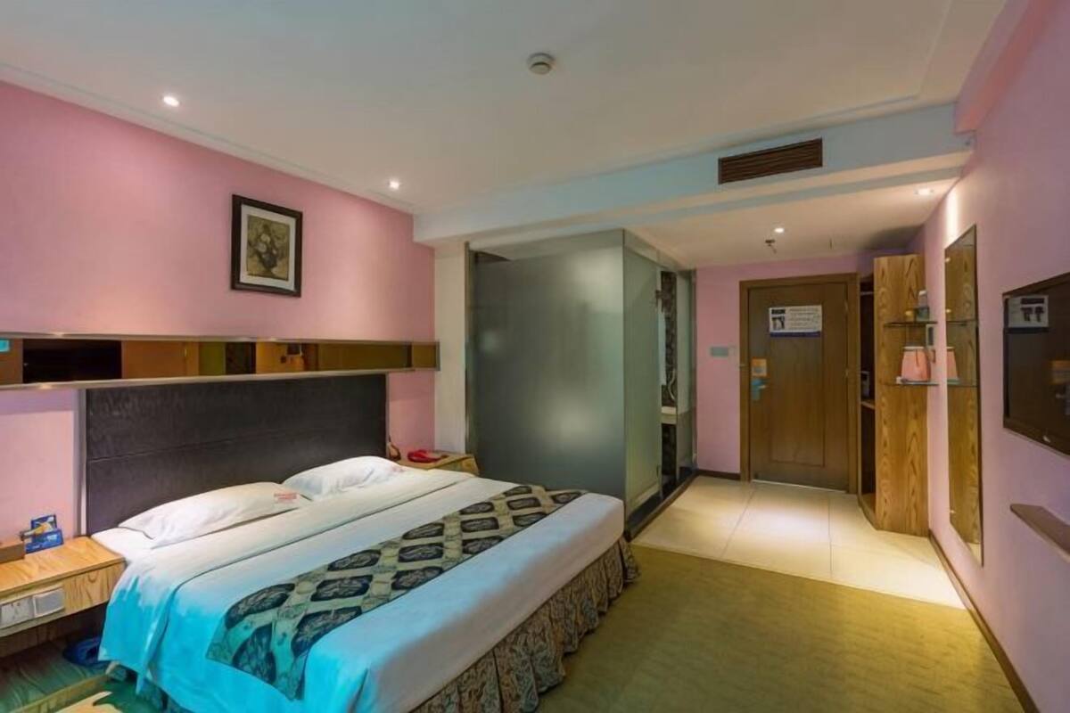 A hotel room with a bed, bedside table, and a door leading to another room.