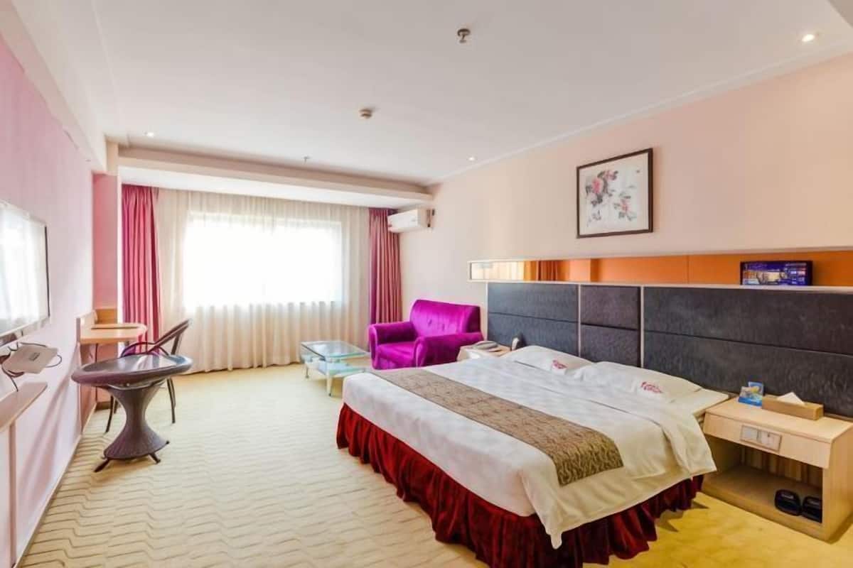 A hotel room with a bed, a desk, a chair, a small table, and a window with curtains.