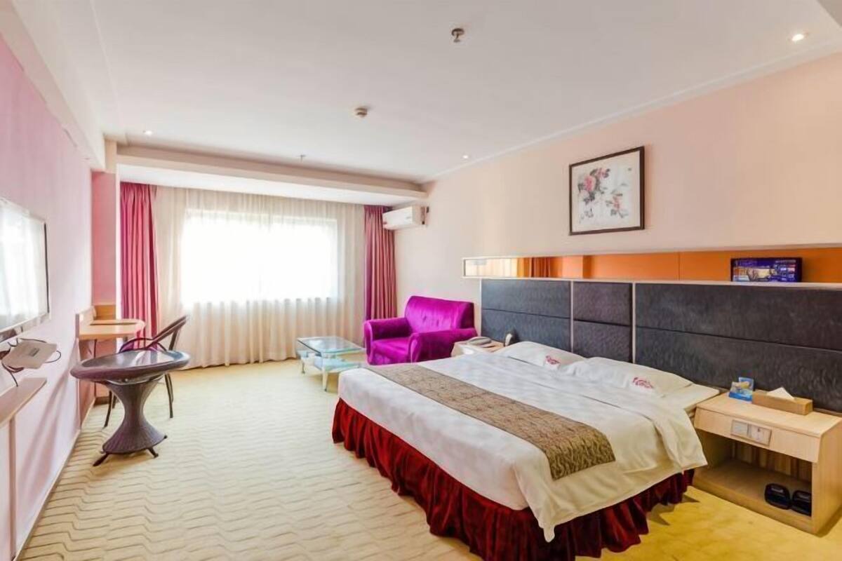 A hotel room with a bed, a desk, a chair, a small table, and a window with curtains.