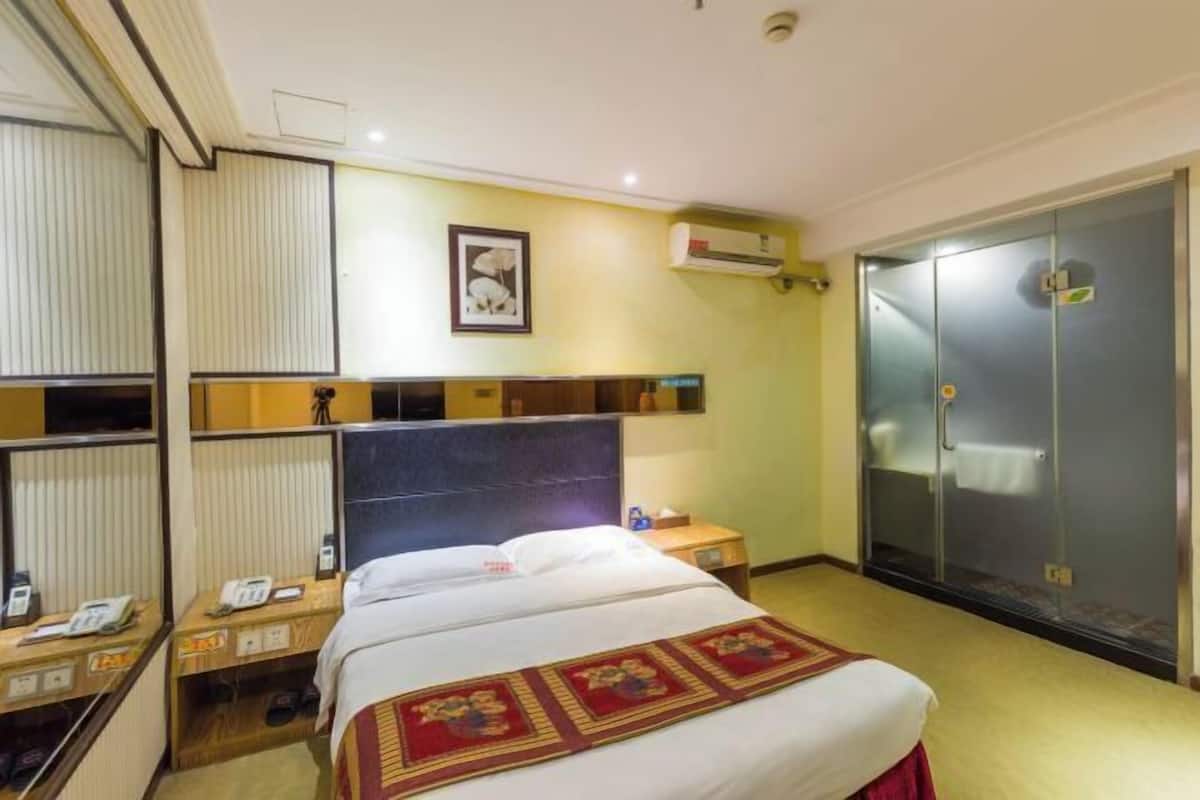 A hotel room with a bed, bedside tables, a wardrobe, and an air conditioning unit.