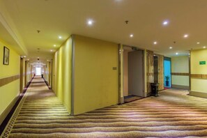 A hotel corridor with carpeted floors, doors on both sides, and a long hallway leading to a bright room. - Jinda Business hotel (Zhuhai)