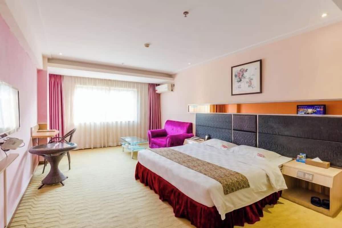A hotel room with a bed, a desk, a chair, a small table, and a window with curtains.