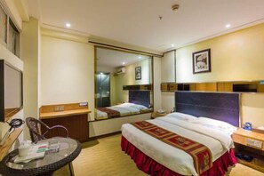 Quarto de hotel com cama, escrivaninha, cadeira, espelho e mesa de cabeceira.