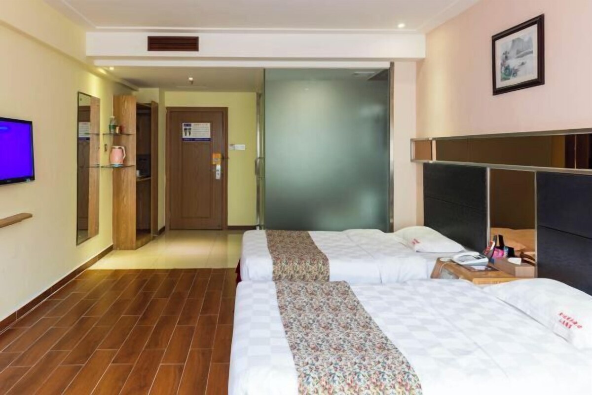 Quarto de hotel com duas camas, uma televisão, um espelho e uma porta que dá para um corredor.