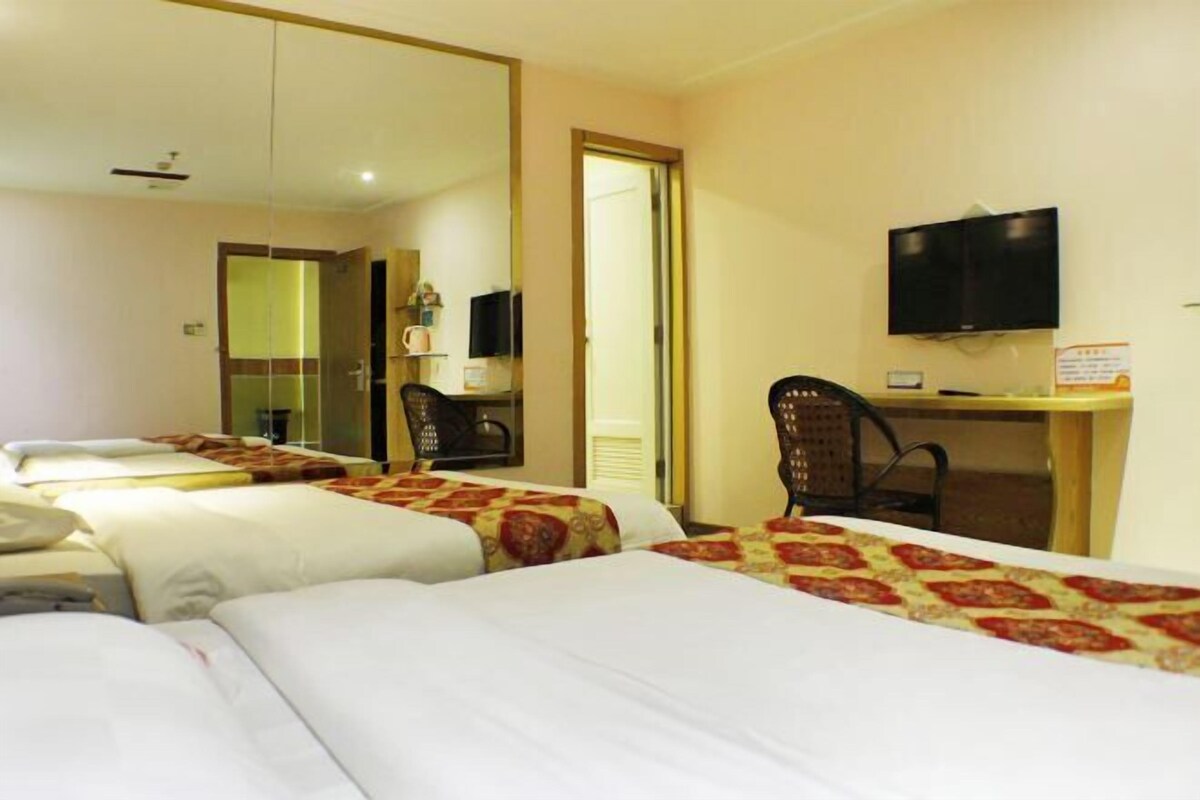 Quarto de hotel com três camas, uma escrivaninha, uma cadeira, uma televisão e um espelho.