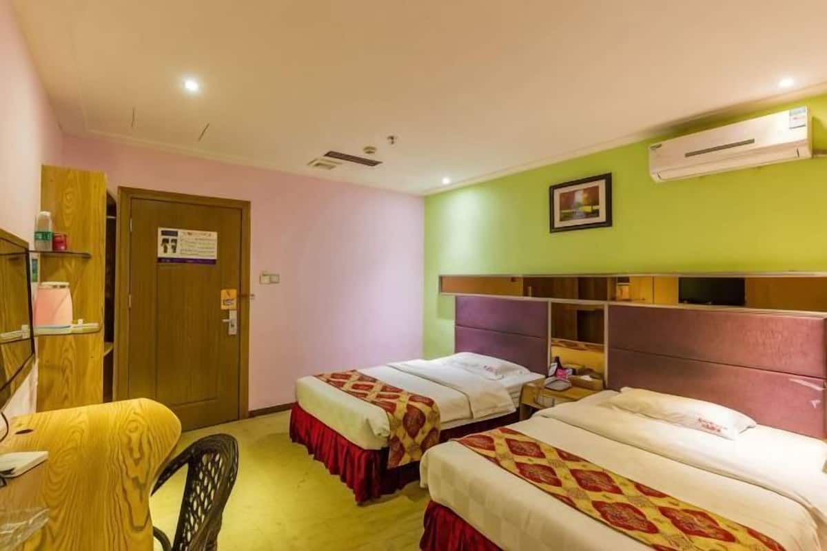A hotel room with two beds, a desk, a chair, a door, and an air conditioning unit.