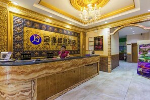 A hotel reception area with a marble counter, a receptionist, and a signboard with hotel name. - Jinda Business hotel (Zhuhai)
