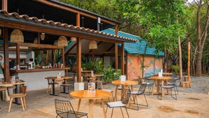 An outdoor cafe with wooden tables and chairs, a covered seating area, and a mural on the building. - Selina River Venao (Las Escobas del Venado)