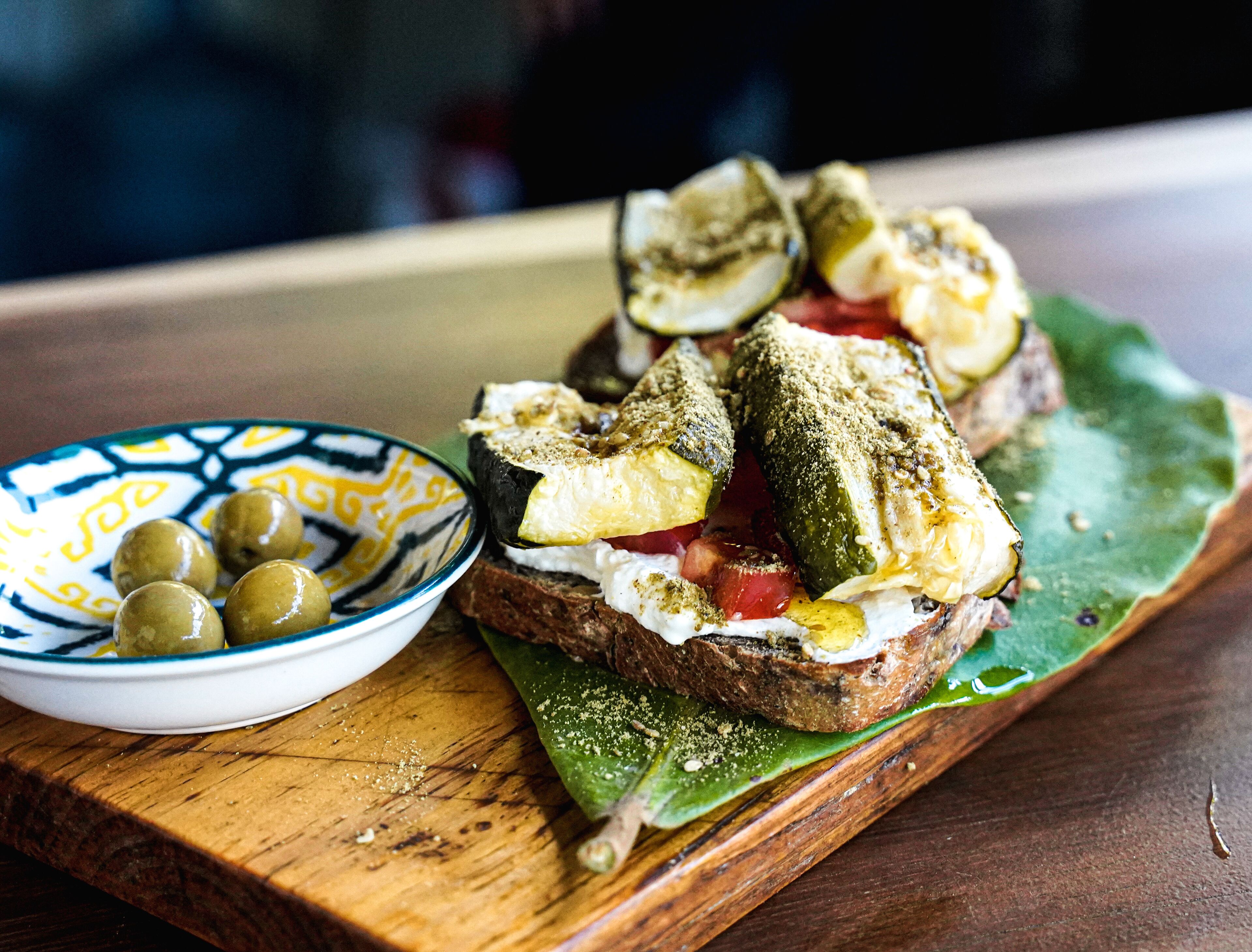 Un panino su un tagliere di legno, con una ciotola di olive accanto.