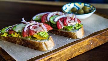Two open-faced sandwiches on a wooden board with a bowl of olives in the background.