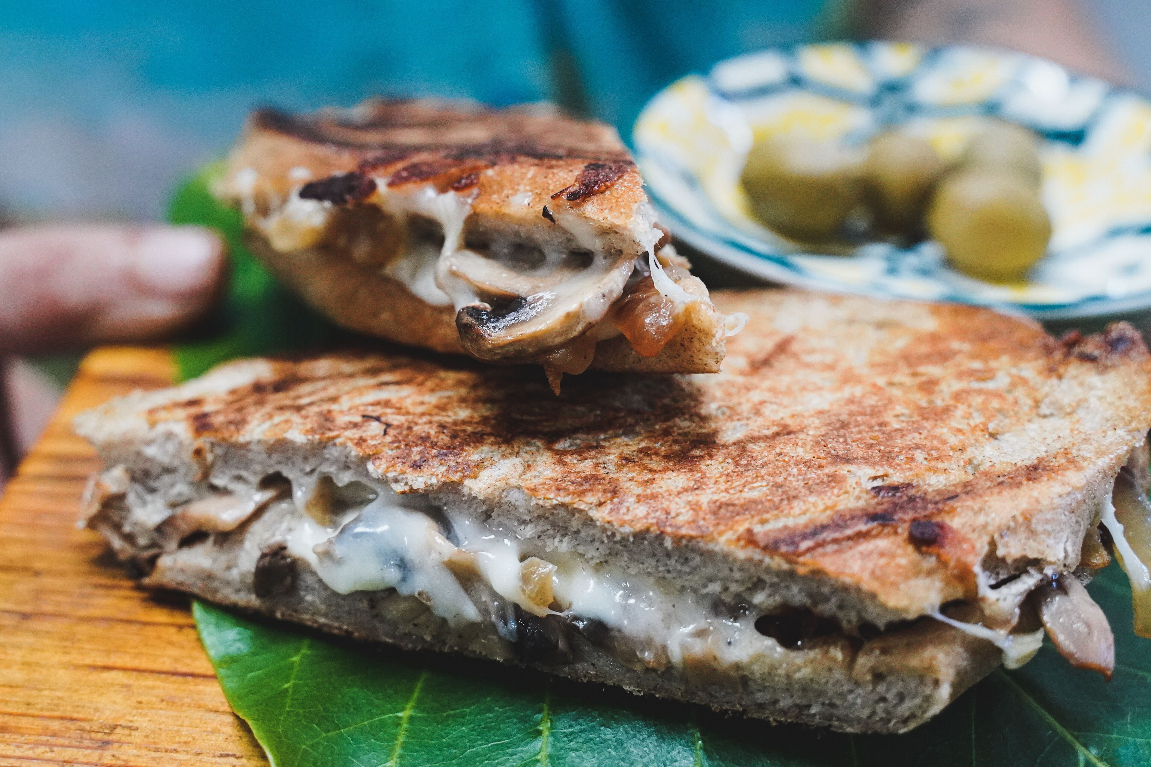 A grilled sandwich with melted cheese and meat, served on a green leaf.