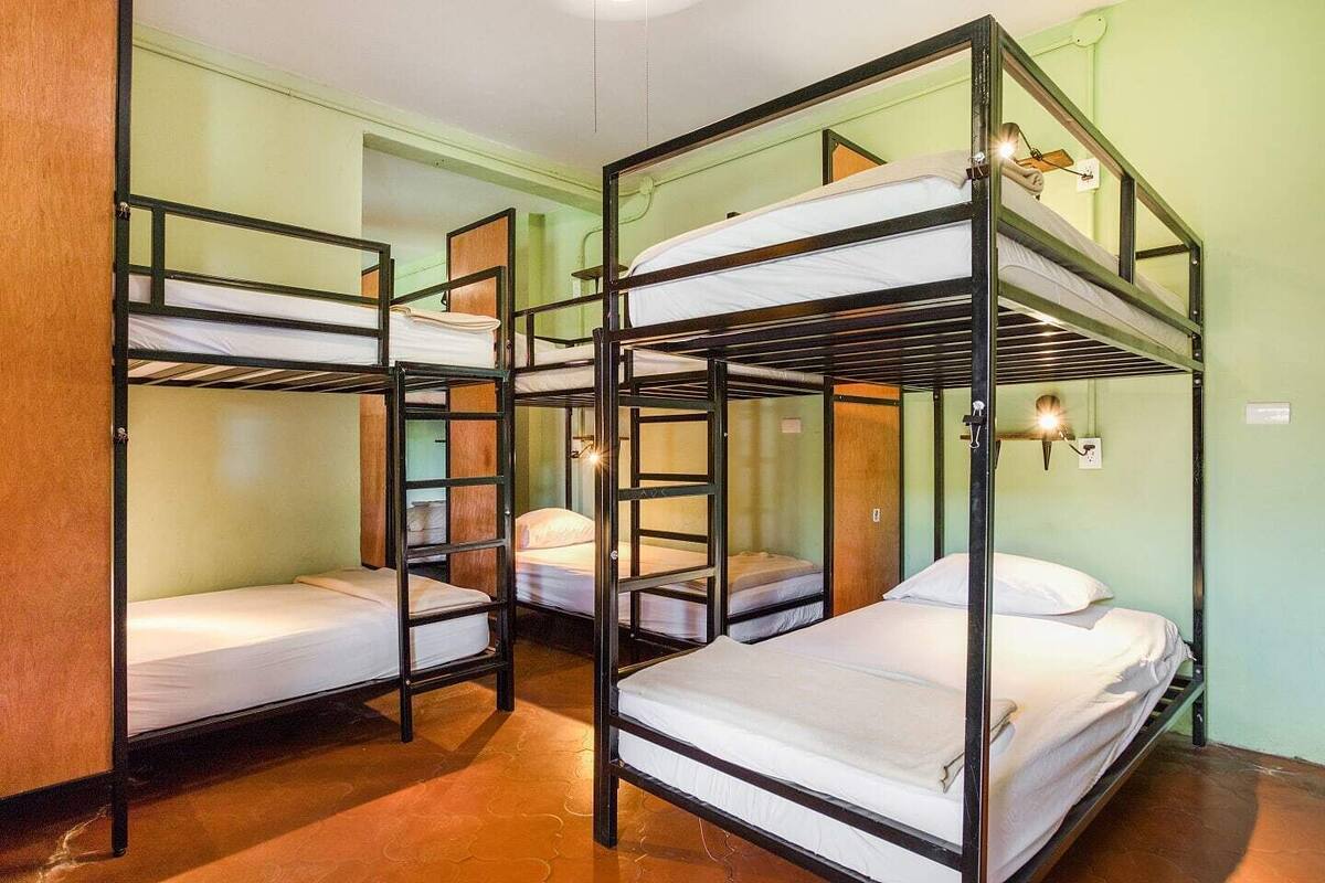 A dormitory room with bunk beds, wooden walls, and a small window.