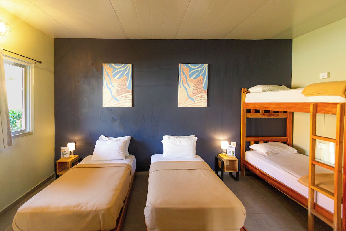 A room with two single beds, a bunk bed, and two wall-mounted paintings.