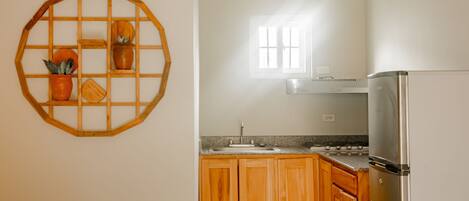 A kitchen with wooden cabinets, a stainless steel refrigerator, a sink, and a window with sunlight streaming in.