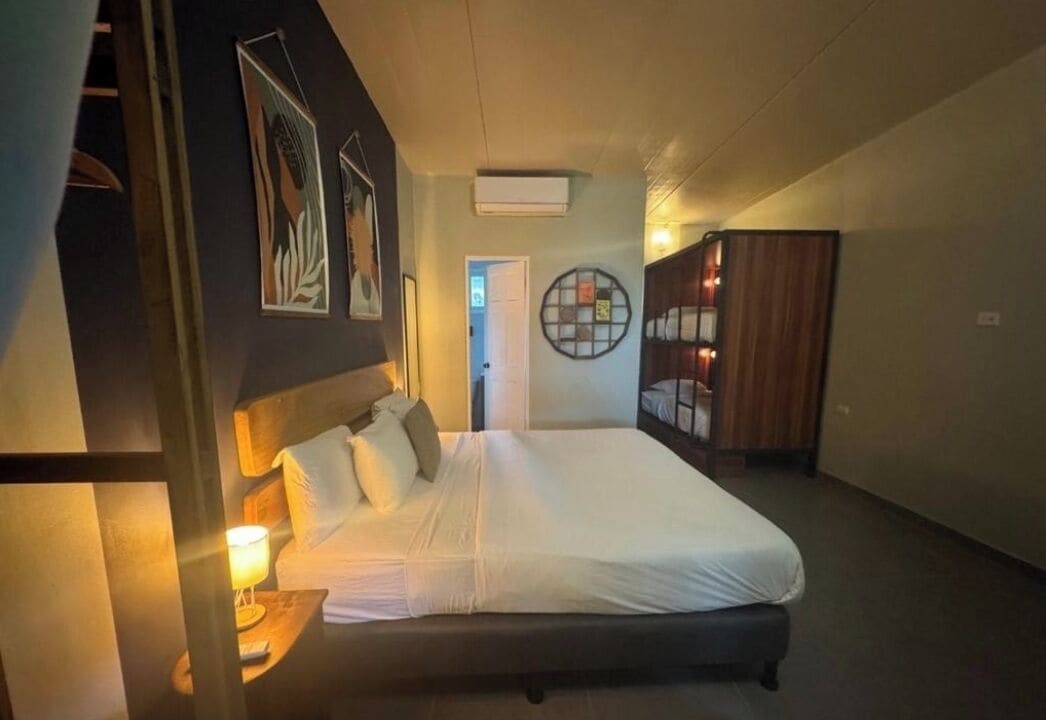 A hotel room with a large bed, a bedside table with a lamp, a wardrobe, and wall art.