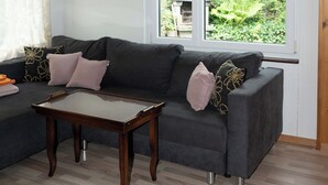 A living room with a dark grey sofa, a wooden coffee table, and a large window with a view of greenery outside.