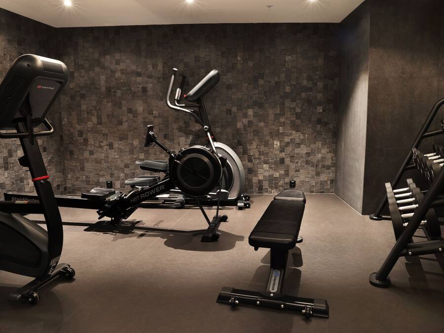 A gym with a stationary bike, elliptical, bench, and weight rack.