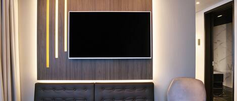 Una sala de estar moderna con un televisor de pantalla plana grande montado en una pared de madera, un sofá marrón oscuro y un sillón gris claro.