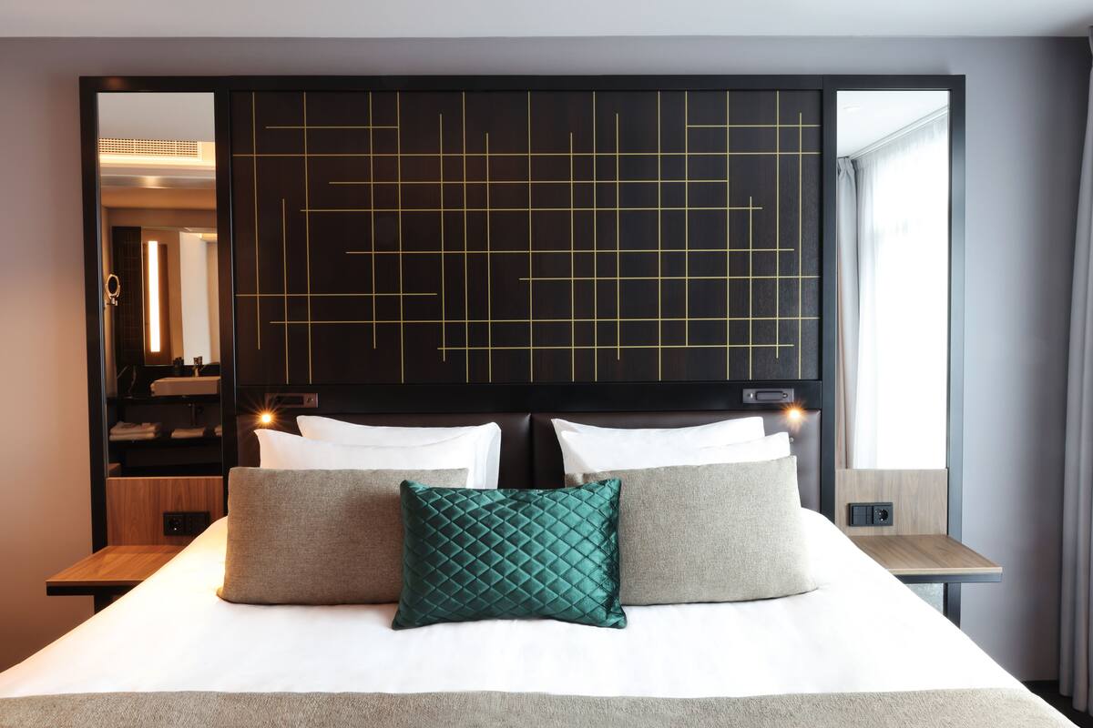 A modern hotel room with a large bed, a headboard with a geometric pattern, and a small bedside table.