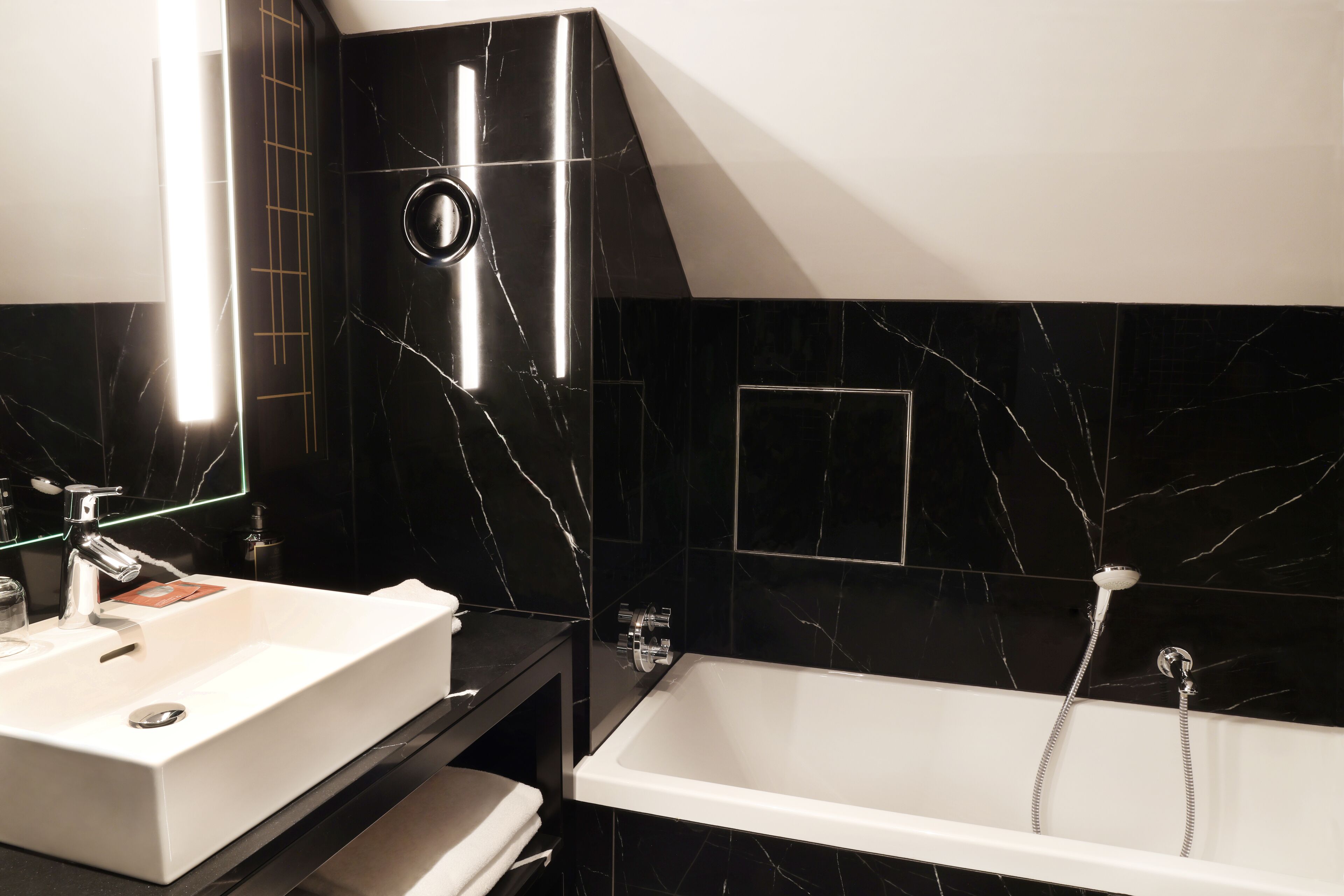 Une salle de bain moderne avec un lavabo blanc, des murs en marbre noir et une baignoire blanche.