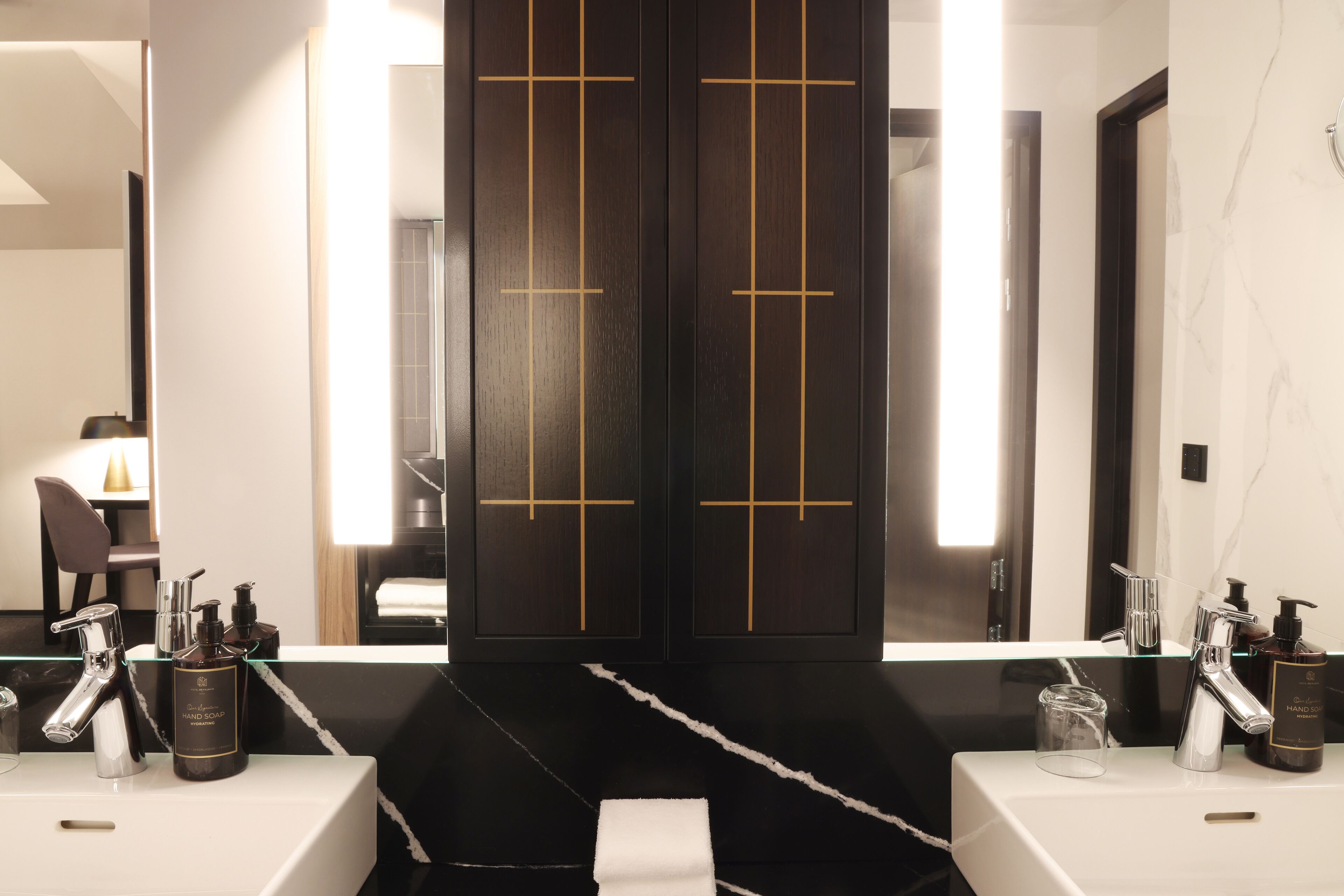 Ein modernes Badezimmer mit zwei Waschbecken, einem großen Spiegel und einer schwarzen Kommode mit goldenen Akzenten.