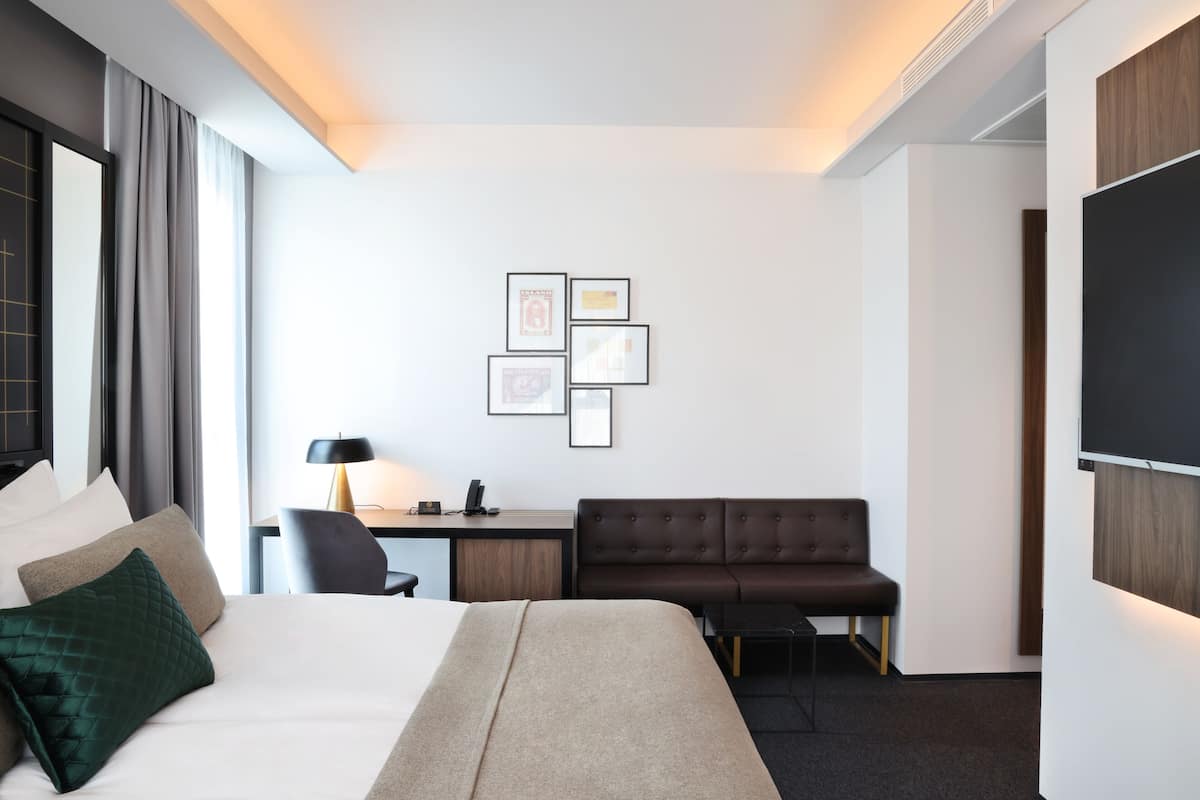 A hotel room with a bed, a desk, a chair, a sofa, and a TV.