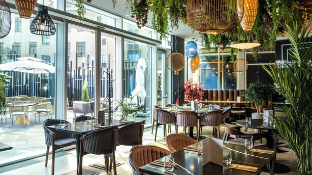 Un restaurante con mesas en el interior, lámparas de mimbre colgantes y vistas de la ciudad a través de amplias ventanas.