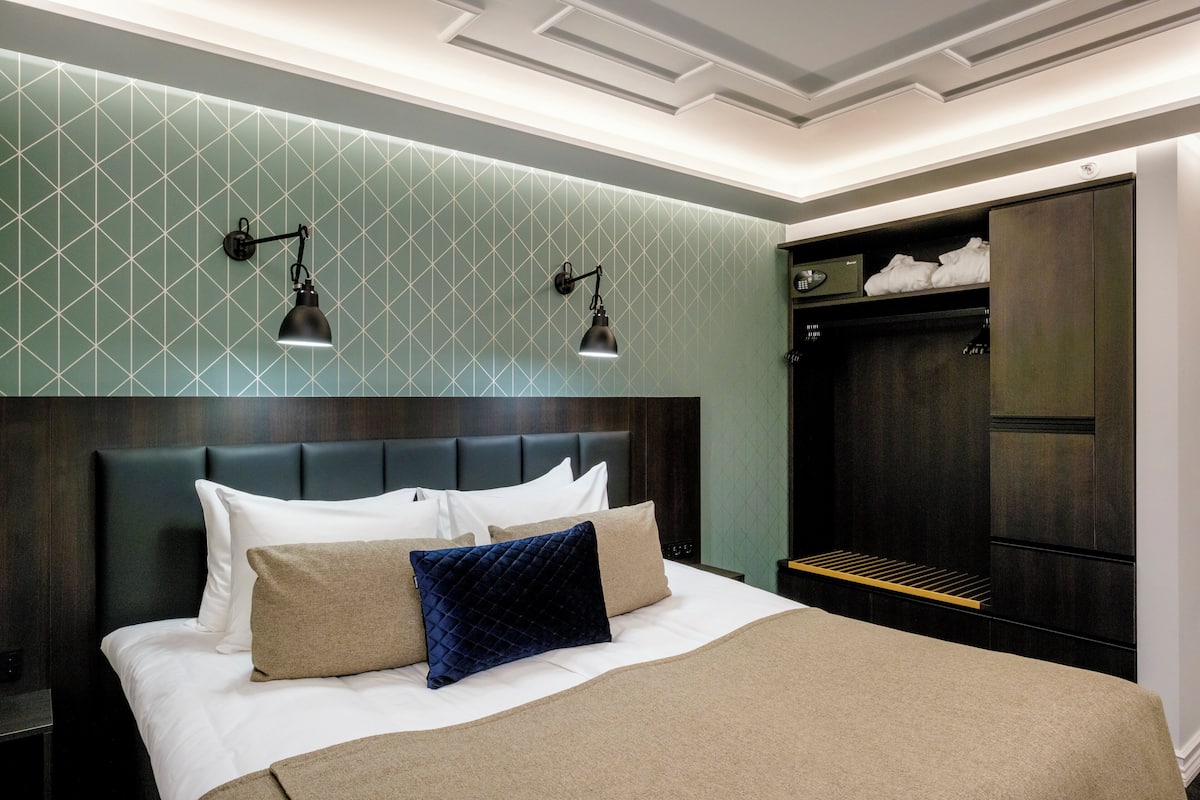 A hotel room with a large bed, dark headboard, two wall-mounted reading lamps, and a wardrobe with a mirror.