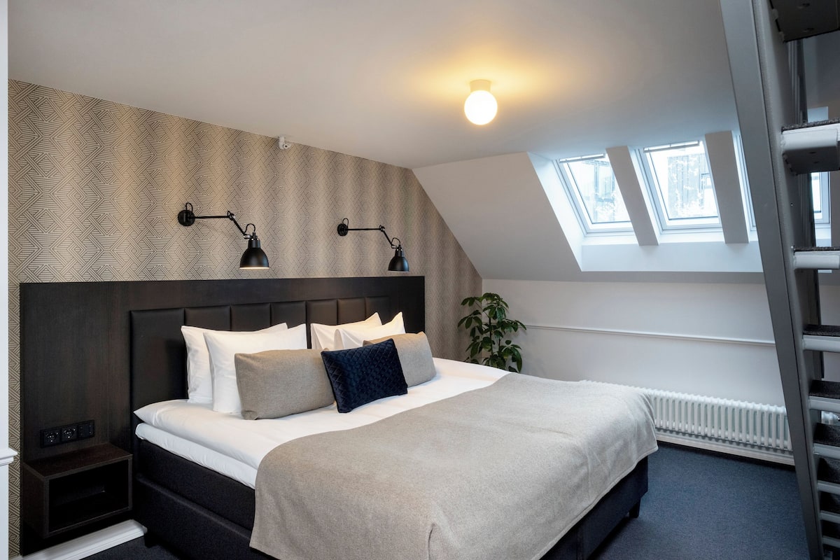A modern bedroom with a large bed, two bedside lamps, a radiator, and skylights.