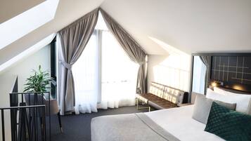 Habitación de hotel moderna con una cama grande, un banco, una planta en maceta y vistas al exterior.