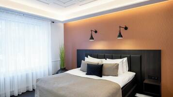A hotel room with a large bed, a headboard, two wall-mounted lamps, and a window with sheer curtains.