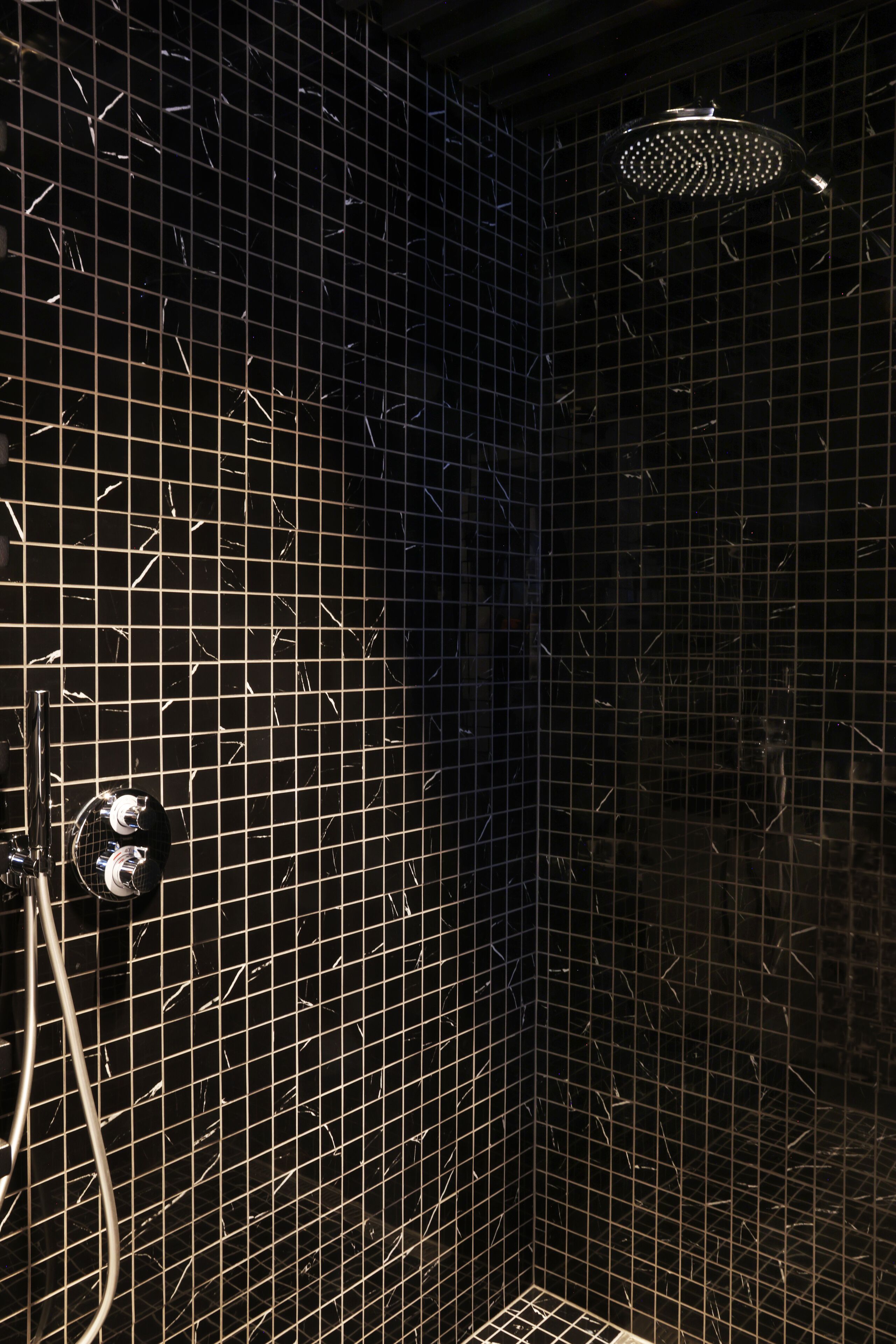 A shower area with a tiled wall and a handheld showerhead.