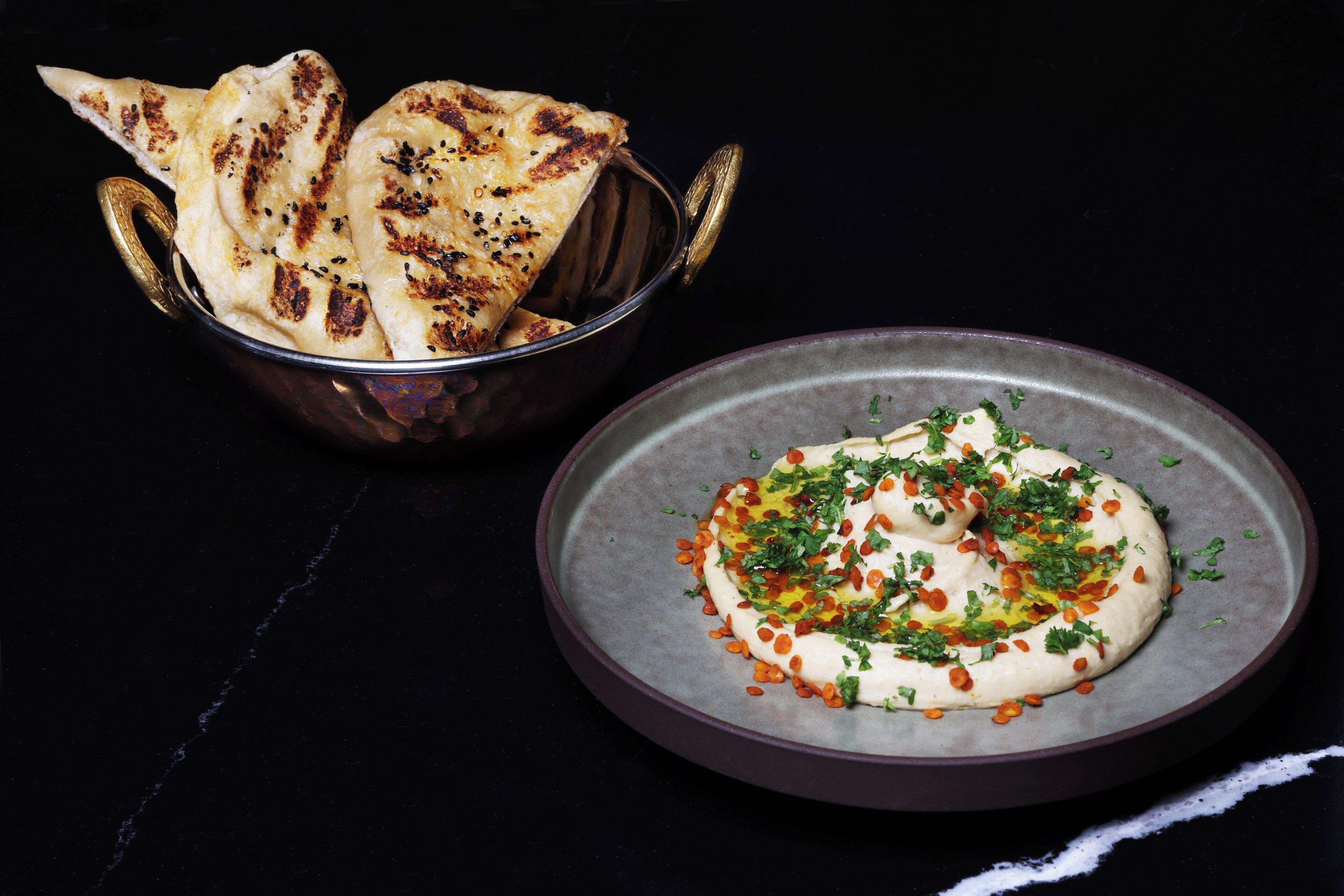A bowl of flatbread and a plate of hummus with herbs and spices.