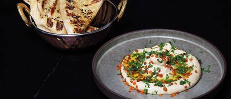 A bowl of flatbread and a plate of hummus with herbs and spices.