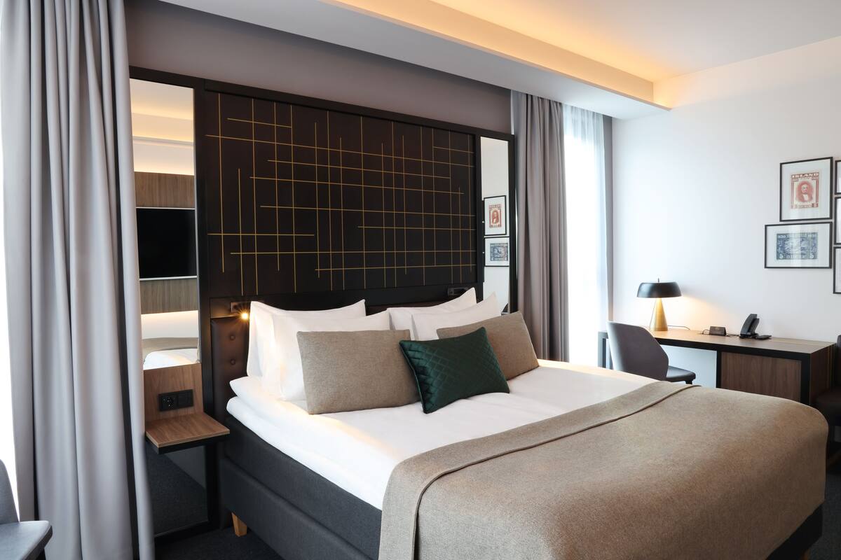 A modern hotel room with a large bed, a desk, and a chair.