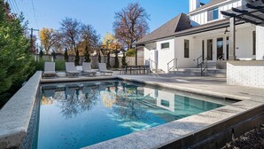 A rectangular swimming pool with a stone edge, surrounded by a patio area with lounge chairs and a covered seating area. - Gathering Place Luxury-Pool/Spa/OutdoorKitchen (Tulsa)