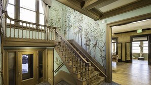 A grand staircase with a wooden handrail and a leopard print carpet, leading to a room with a large window and a door with frosted glass panels. - The Edward Hotel (Buffalo)