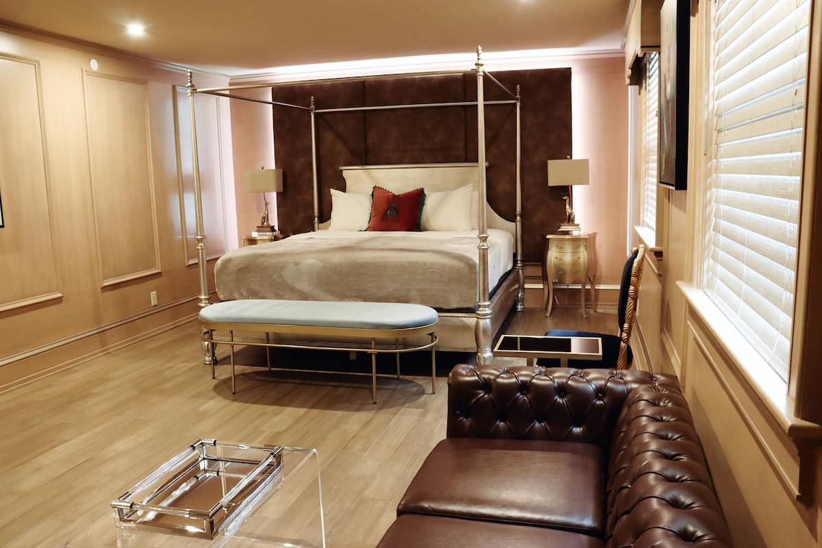 Un dormitorio espacioso con cama con dosel, un banco, una mesita y un sofá.