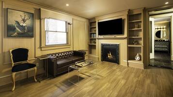 A living room with a leather sofa, a glass coffee table, a flat-screen TV, a fireplace, and a bookshelf.