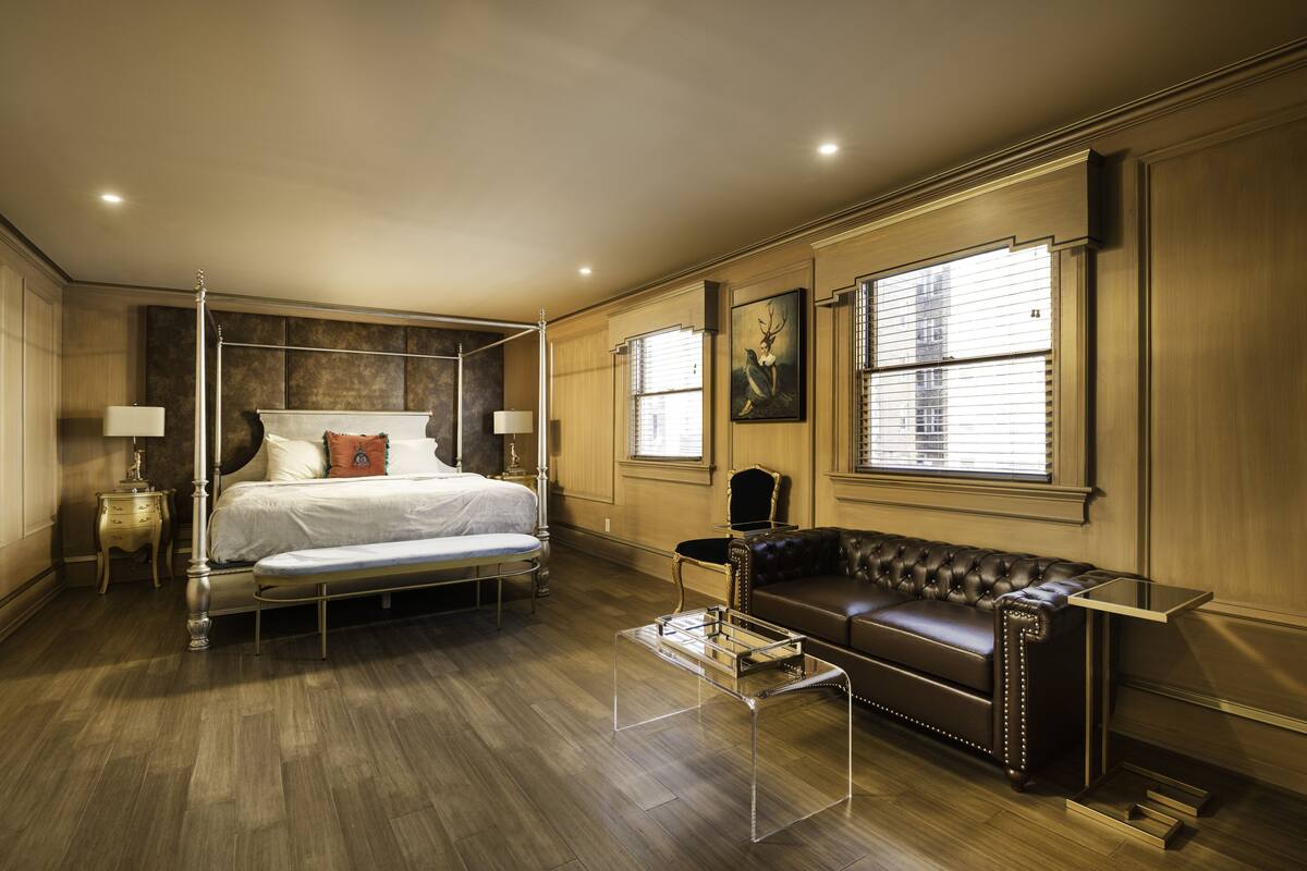Un espacioso dormitorio con una cama con dosel, un sofá de cuero y una mesa de centro de vidrio.