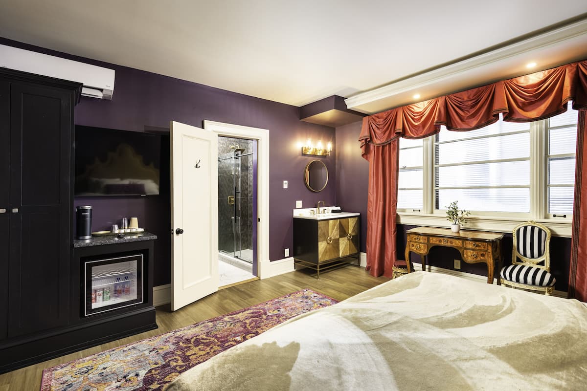 Un dormitorio con cama, cómoda, tocador, silla y ventana con cortinas.