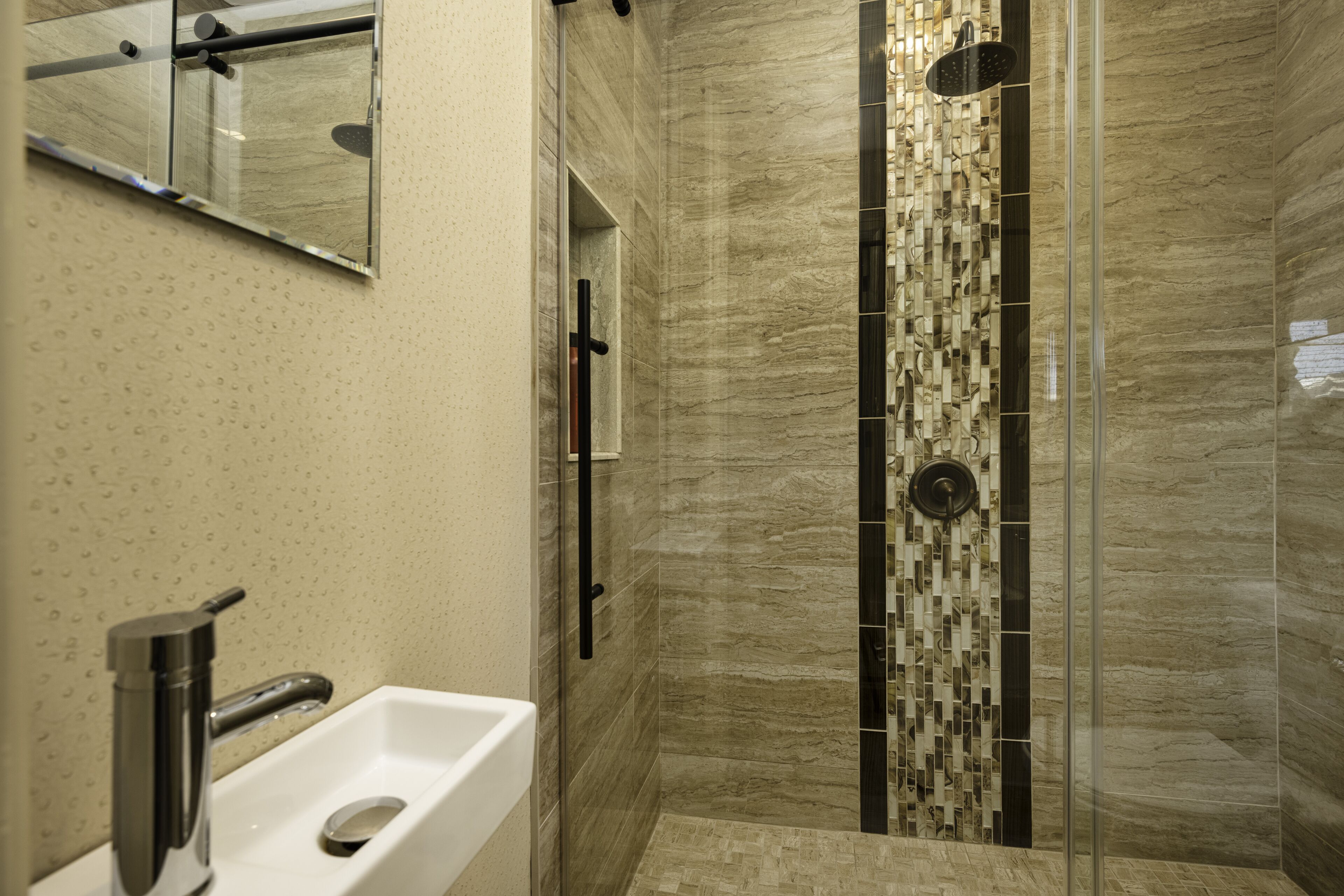 A modern bathroom with a white sink, a glass shower enclosure, and a tiled wall with a geometric pattern.