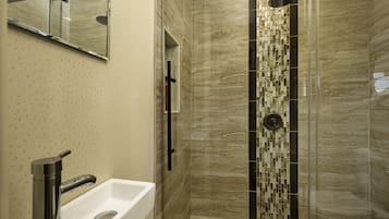 A modern bathroom with a white sink, a glass shower enclosure, and a tiled wall with a geometric pattern.
