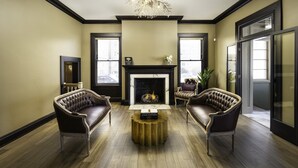 A living room with a fireplace, two leather armchairs, a coffee table, and a chandelier. - The Edward Hotel (Buffalo)