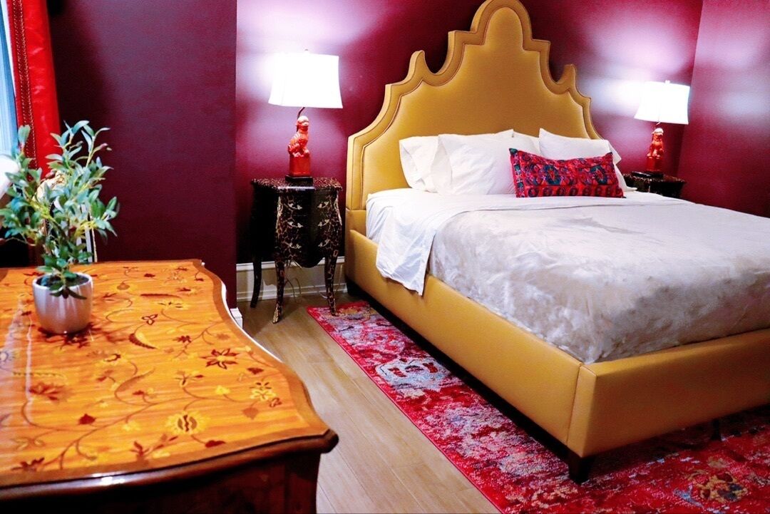 A hotel room with a yellow bed, white bedding, a red and white patterned rug, and two nightstands with lamps.