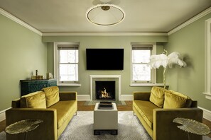 A living room with two yellow sofas, a white coffee table, a fireplace, and a flat-screen TV mounted above the fireplace. - The Edward Hotel (Buffalo)