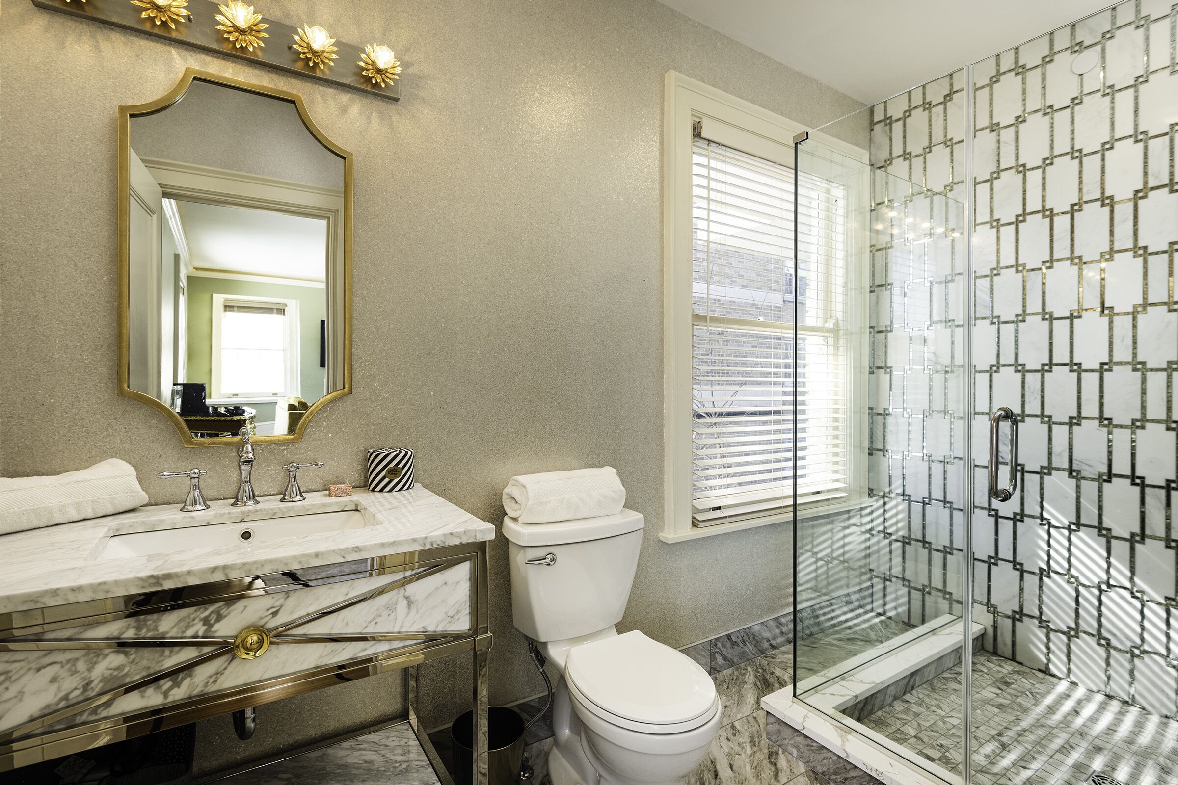Ein Badezimmer mit Marmor-Waschtisch, Toilette und einer Duschkabine aus Glas.