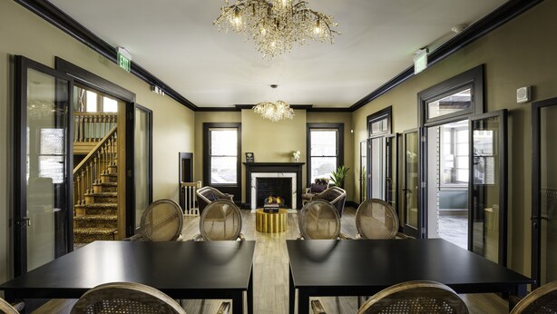 A spacious dining area with a long table, multiple chairs, a chandelier, and a fireplace. - The Edward Hotel (Buffalo)