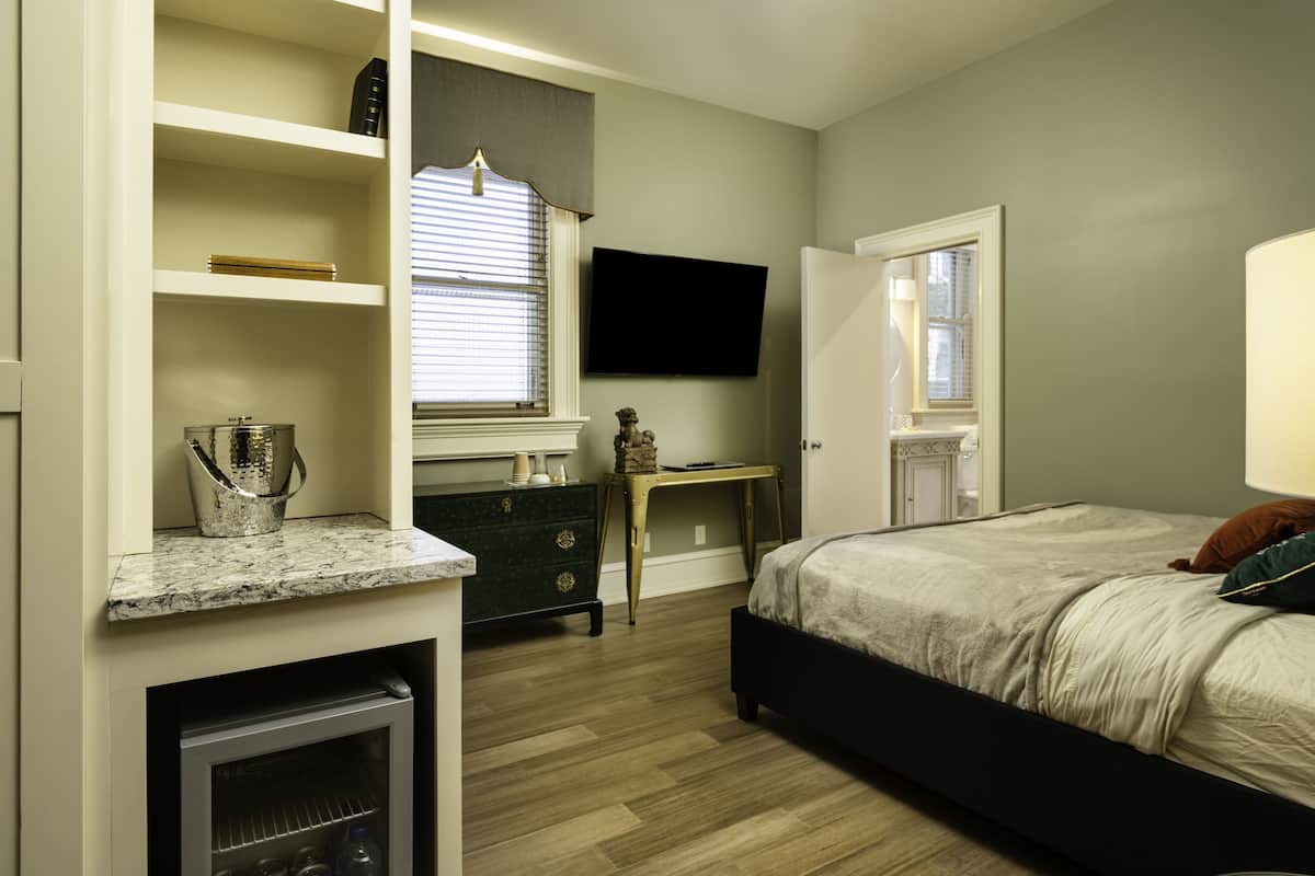 Un dormitorio con cama, escritorio, televisor y refrigerador empotrado.